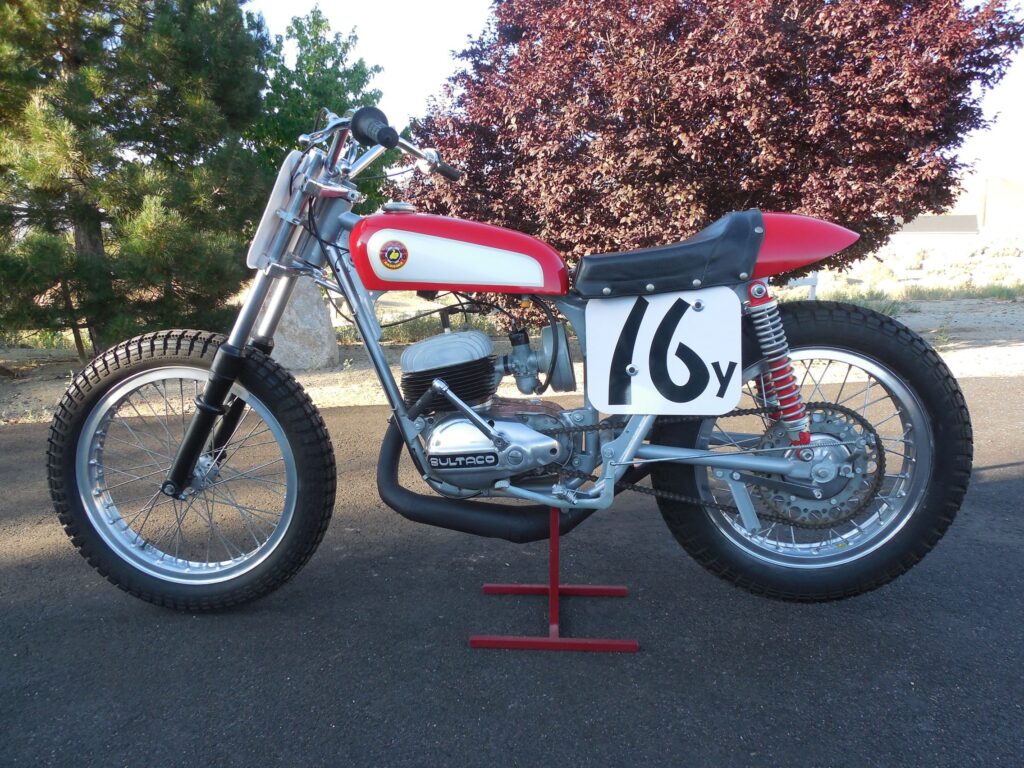 Vintage Bultaco flat tracker with a white number 16 plate on a red stand