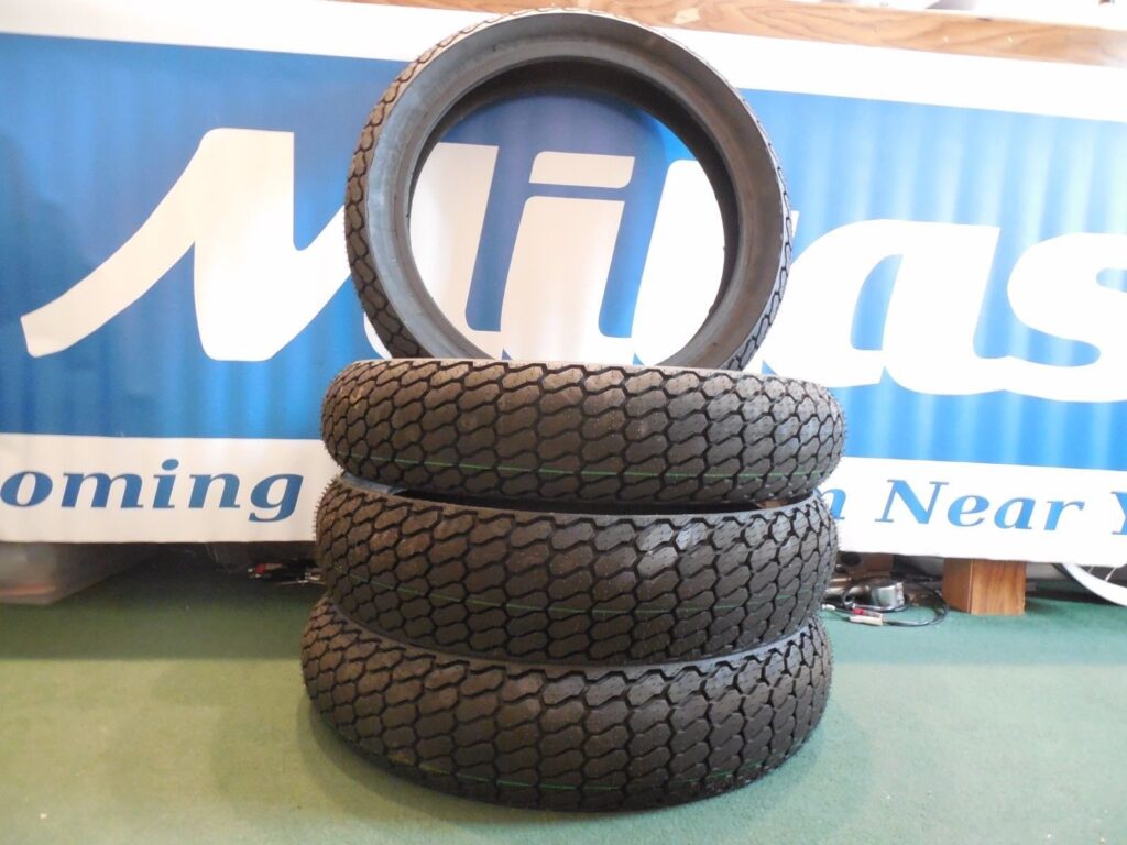 A stack of Mitas flat track tires in front of a Mitas banner