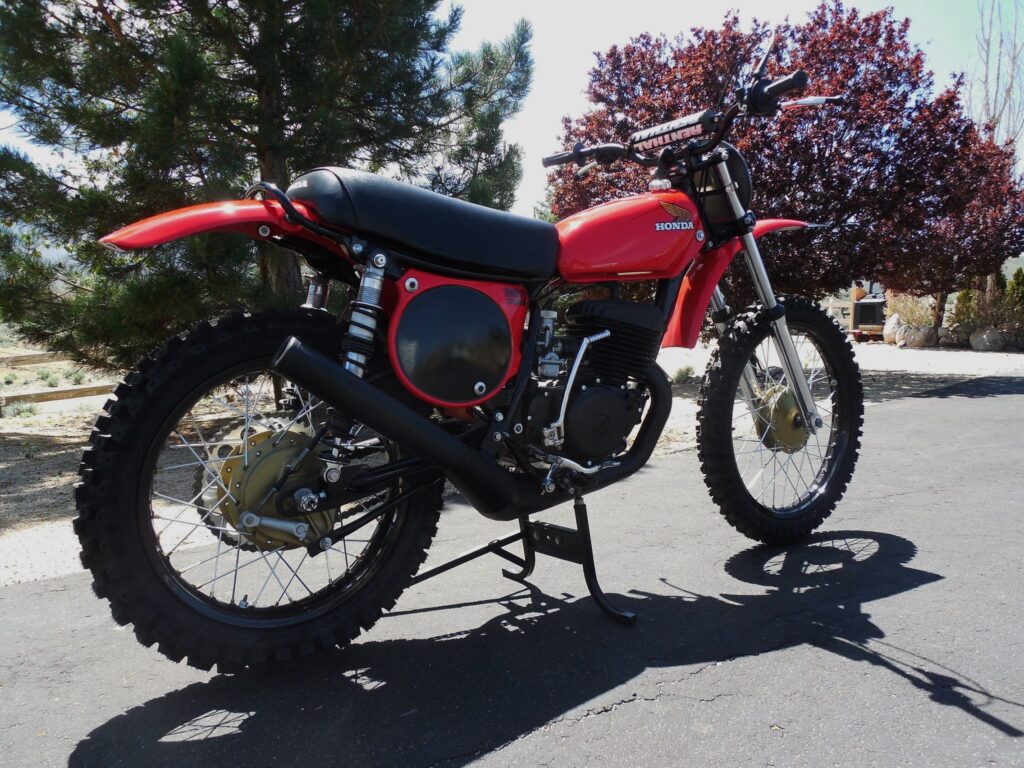 Red vintage dirt bike with red side panels and a black seat on a stand